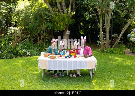 Felice afroamericano fratelli e nonni in coniglietto orecchie pittura uova di pasqua in cortile. Inalterato, stile di vita, giorno di pasqua, arte, celebrazione, f Foto Stock