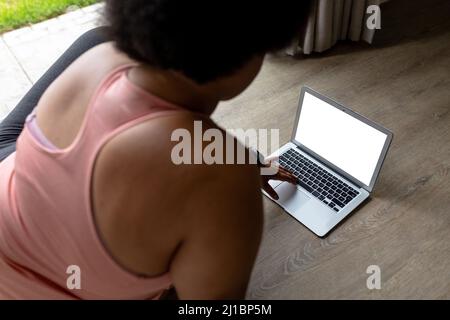 Vista posteriore della donna afroamericana per adulti di media età che usa un computer portatile mentre si esercita a casa Foto Stock