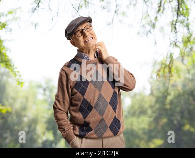 Uomo anziano che gli fa il collo in un parco con alberi Foto Stock