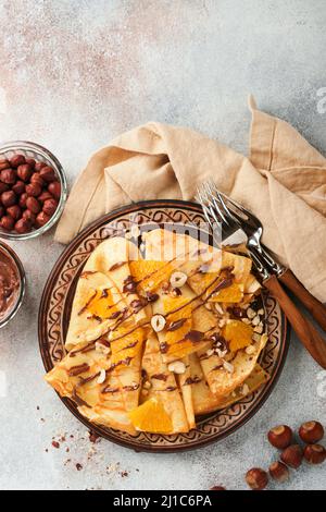 Crepes suzette con arance e cioccolato. Crepes sottile con cioccolato spalmato, nocciole e fette d'arancia frutta in piatto per colazione su cemento vecchio Foto Stock