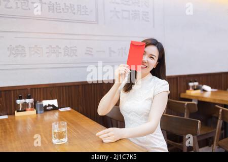 Bella giovane donna asiatica in abito bianco tradizionale chiamato cheongsam seduta in ristorante giapponese o caffetteria e in attesa di cibo ordinato. Ragazza Foto Stock