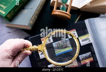 Mosca, Russia, Marzo 2022: Hobby - raccolta di francobolli. Guardando il vecchio timbro di post sfocato attraverso la lente di ingrandimento. Spazio di copia. Vecchi libri, clessidra. Foto Stock