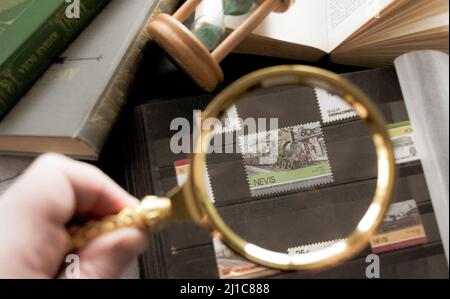 Mosca, Russia, Marzo 2022: Hobby - raccolta di francobolli. Guardando un francobollo di 60 cent di Nevis con locomotiv attraverso una lente d'ingrandimento dorata. Vecchi libri Foto Stock