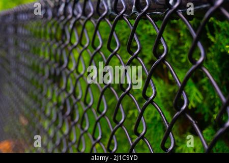 Una fence di collegamento di catena nera fotografata da una prospettiva creativa per dare la profondità dell'immagine. Foto Stock