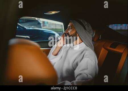 Uomo Saudita seduto in auto e al telefono Foto Stock