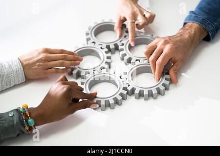 Un gruppo di imprenditori di unire insieme ingranaggi sul tavolo al posto di lavoro Foto Stock