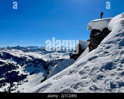 Freerider in piedi su una scogliera innevata vicino al bordo godendo di spettacolari vedute delle Alpi austriache. Vorarlberg, Austria. Foto Stock