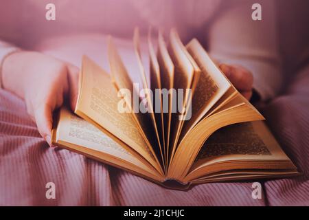 Un uomo è sdraiato su un letto con una morbida coperta rosa e flipping attraverso le pagine di un vecchio libro interessante. Lettura della documentazione. Autosviluppo. Foto Stock