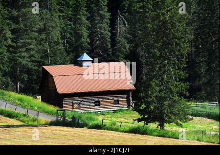 Il vecchio fienile in tronchi è stato restaurato aggiungendo un nuovo tetto in stagno. Il granaio si trova ai piedi delle montagne di Absaroka nel Montana. Corsia di campagna Wanders acros Foto Stock