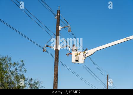 Un operatore di costruzioni elettriche o un lineman che lavora in una benna rialzata per eseguire nuove linee di trasmissione elettrica. Foto Stock