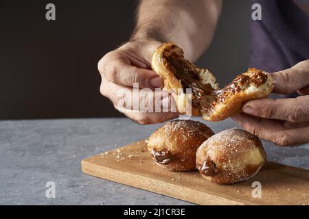 Un primo piano delle mani di un uomo che si rompono in un berliner mezzo dolce ripieno di dulce de leche Foto Stock