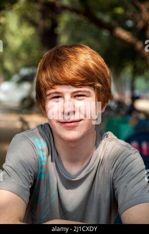 ragazzo con capelli rossi e piccone in faccia sembra felice e mantiene le braccia incrociate Foto Stock