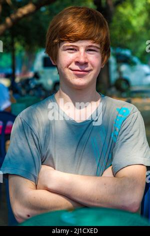 Ragazzo con i capelli rossi e piccone in faccia sembra felice e keepts le braccia incrociate Foto Stock