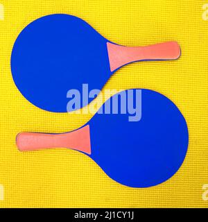 Ci vogliono due volte per il tango. Scatto ad angolo alto di due racchette da ping-pong blu poste su uno sfondo giallo all'interno di uno studio. Foto Stock