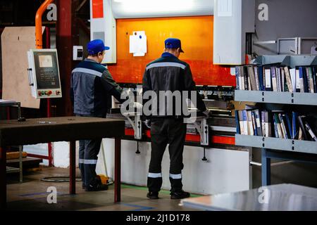 Operatori tecnici che lavorano con lamiera su pressa idraulica CNC. Foto Stock