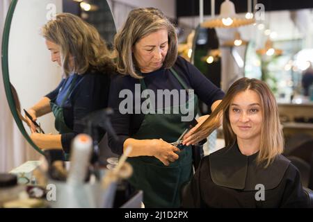 Giovane donna che ottiene il taglio di capelli da anziana donna parrucchiere Foto Stock