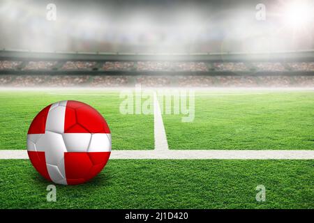 Football in uno stadio all'aperto luminoso con bandiera della Danimarca dipinta. Mettere a fuoco su primo piano e palla di calcio con profondità di campo poco profonda sullo sfondo A. Foto Stock