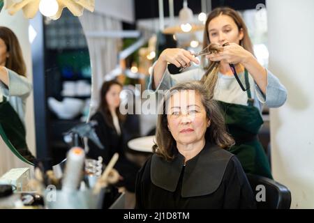 Parrucchiere taglio capelli di donna anziana in salone Foto Stock