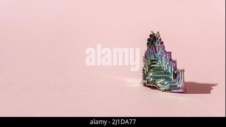 Bismuto sintetico BismuthumCrystal con film di ossido iridescente su sfondo rosa close up isolato. Incredibile colorata pietra Gemstone arcobaleno brillante Foto Stock