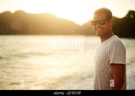 Non è un posto migliore della spiaggia. Ritratto di un bel giovane uomo in piedi sulla spiaggia al tramonto. Foto Stock