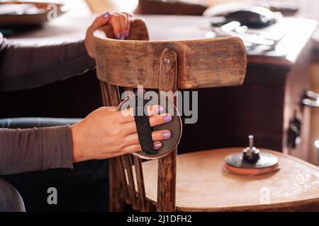 Primo piano delle mani rimozione del vecchio strato di vernice levigatura superficie di sedia antica con carta vetrata speciale in officina domestica. Pratiche sostenibili. Riutilizzo di Foto Stock