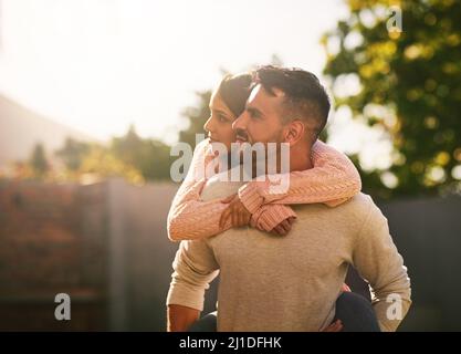 I giorni brillano con amore in loro. Scatto di una giovane coppia felice godendo un giro di piggyback all'aperto. Foto Stock