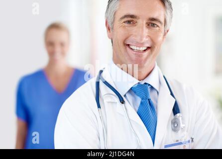 La salute dei nostri pazienti è tutto ciò che conta. Ritratto di un medico maschile con un collega in piedi sullo sfondo. Foto Stock