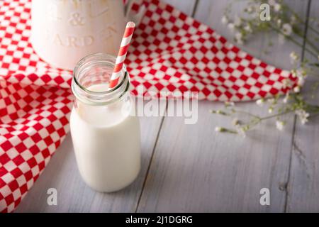 Latte fresco in contenitore di vetro con paglia di carta bianca e rossa biodegradabile su superficie bianca rustica in legno Foto Stock