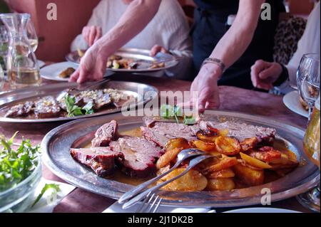 Vari piatti con incontro arrosto, patate e verdure su tavola rustica nel ristorante Foto Stock