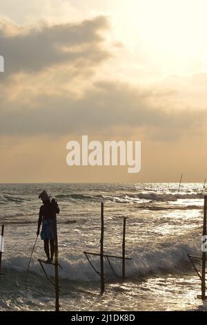 Silhouette di pescatore su palafitte al tramonto, costa meridionale dello Sri Lanka Foto Stock