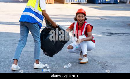 African american donna caposquadra o operaio di manutenzione messo su caschi di sicurezza mano che tiene garbage nero sacchetto e la collaborazione che mette il wast di garbage di plastica Foto Stock