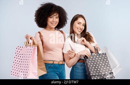 Fai shopping fino a che non cadremo. Studio ritratto di due giovani donne che portano un mazzo di borse shopping. Foto Stock