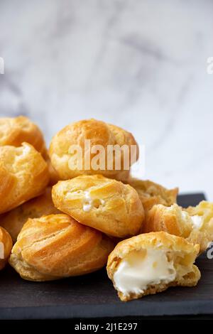 Profiteroles fatti in casa ripieni di panna montata su sfondo chiaro di marmo. Foto Stock