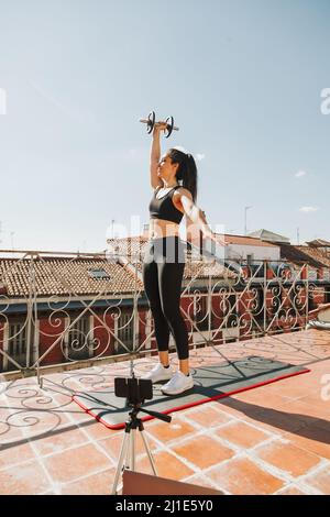 Giovane allenatore sportivo donna che fa lezioni online tramite videochiamata sul suo cellulare lezioni di streaming e concetto di stile di vita sanitario Foto Stock