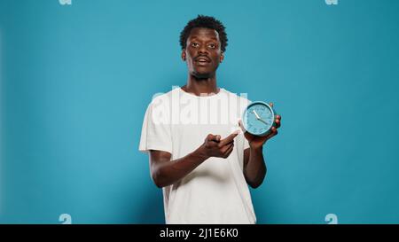 Persona casual che punta all'ora sulla parete orologio per ora e minuti. Ritratto del giovane uomo che guarda l'orologio e spiega il conto alla rovescia e il ritardo per il lavoro. Allarme di impostazione puntuale per adulti Foto Stock