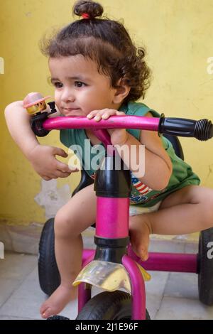 Carino ragazzo Shivaay che guida in bicicletta a casa balcone durante l'estate, dolce bambino fotoshoot durante la luce del giorno, ragazzo piccolo godere in bicicletta a ho Foto Stock