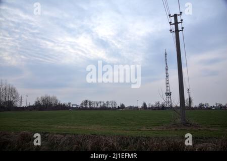 Campo coltivato in una giornata nuvolosa al crepuscolo con una torre radio in lontananza Foto Stock