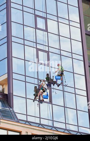 Lavoratori di alpinismo industriale lavano finestre in vetro di un alto edificio, appesi su funi di arrampicata di sicurezza. Due pulitori per finestre uomini che lavorano insieme all'esterno del grattacielo. Foto Stock