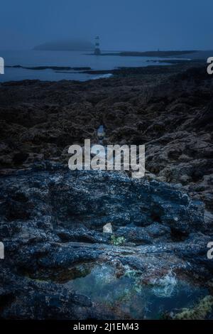 Blue Hour sulla spiaggia rocciosa vicino a Penmon Point sull'isola di Anglesey nel Galles del Nord. Mare scuro e malvagio, ottimo per la copertina dei libri. Foto Stock