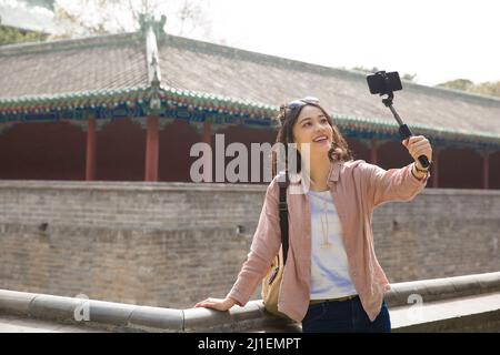 Giovane turista femmina che prende un selfie accanto ad un antico corridoio cinese - foto di scorta Foto Stock