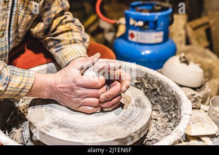 Mani muscolari di uomo di mezza età, vasaio, sporcato in argilla, forma ceramica da argilla sulla ruota del vasaio Foto Stock