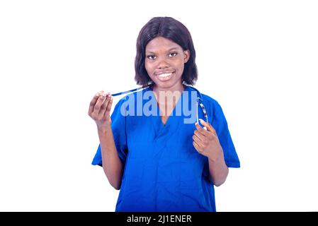 una giovane infermiera in uniforme in piedi su uno sfondo bianco regolando il suo stetoscopio e guardando la telecamera sorridendo Foto Stock