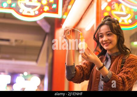 Giovane studentessa universitaria femminile ammirando la figura di zucchero di calabash ad un mercato notturno a Pechino - foto di scorta Foto Stock