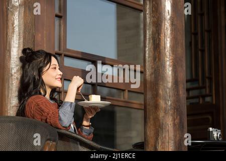 Studente universitario cinese che gusta il tè pomeridiano nel caffè sul marciapiede - foto di scorta Foto Stock