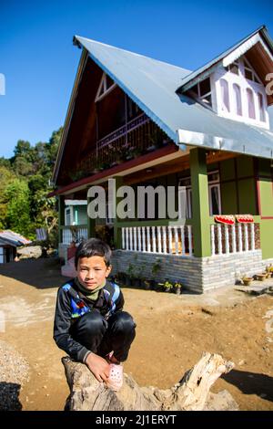 Vista di un ragazzo seduto su un ceppo di albero fuori casa in un villaggio vicino a Pelling. Foto Stock