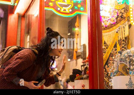 Giovane ragazza cinese del college marveling accanto a mostra finestra di Peking Opera costumi e headdresses - foto di scorta Foto Stock