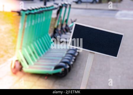 Modello mockup vuoto etichetta lavagna contro gli scooter elettrici parcheggiati sulla strada della città. Servizio self-service di noleggio di mezzi di trasporto su strada. Affitto urbano Foto Stock