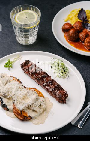 Kebab vegetariano di carne a base di piante con patate dolci, salsa cremosa e parmigiano. Pasta con polpette vegane sullo sfondo Foto Stock
