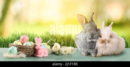 Bellissimo biglietto d'auguri con uova di Pasqua, fiori e coniglietti carini in giardino Foto Stock