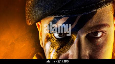 Foto del soldato militare ucraino dipinto faccia in beretta nera uniforme su sfondo bruciato. Foto Stock
